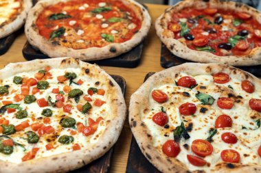 Bir İtalyan restoranında ahşap bir masada bir sürü yeni hazırlanmış pizza.