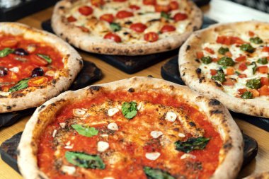 Bir İtalyan restoranında ahşap bir masada bir sürü yeni hazırlanmış pizza.