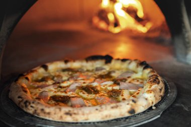 Yanan odun sobasının arka planında taze pişmiş pizza.