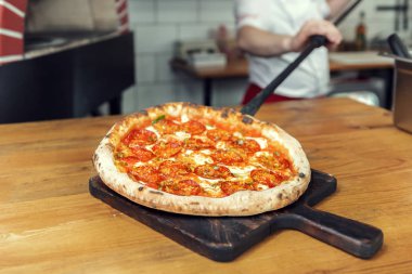 adam bitmiş pizza fırından pizza küreği ile bastırıyor.