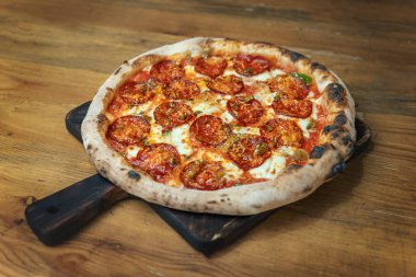 Tahta bir masada salamlı, peynirli, soslu, sebzeli ve etli taze pişmiş pizza.