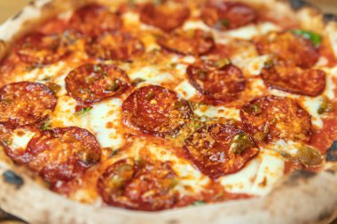 Tahta bir masada salamlı, peynirli, soslu, sebzeli ve etli taze pişmiş pizza.