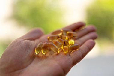 Bir avuç dolusu D vitamini kapsülü bir adamın elinde. Yeşilliğin bulanık arkaplanı