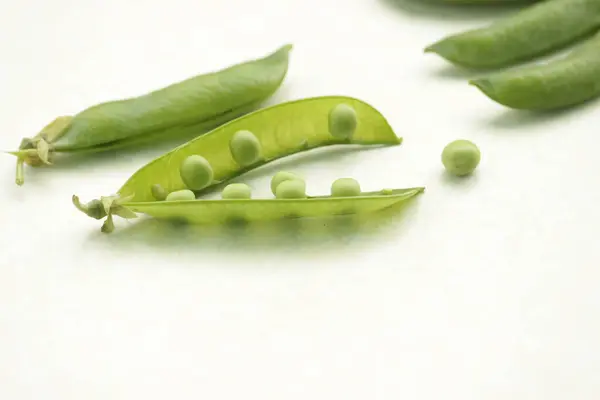 Concept d'alimentation saine. Des gousses de pois verts s'accrochent sur fond blanc . — Photo