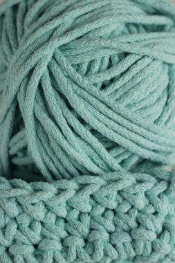 Örgü ve el örgüsü konsepti. Örülmüş bir ürünün bir parçası ve bir kordon topu. Tiffany renk ipliği arka planı.