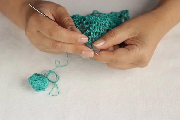 Tricot et crochet à main concept. Les mains des femmes tricotent une serviette verte avec un petit crochet du fil de coton. Fond blanc. Vue supérieure avec espace de copie . — Photo