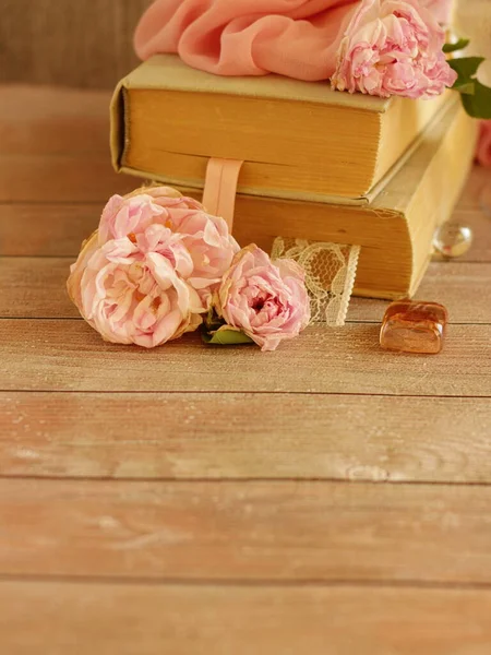 Pink roses, old books, pink silk fabric and glass decor on wooden table.Beautiful romantic composition on woody backdrop.Greeting card for wedding, valentines day or anniversary. copy space for text. — Stockfoto