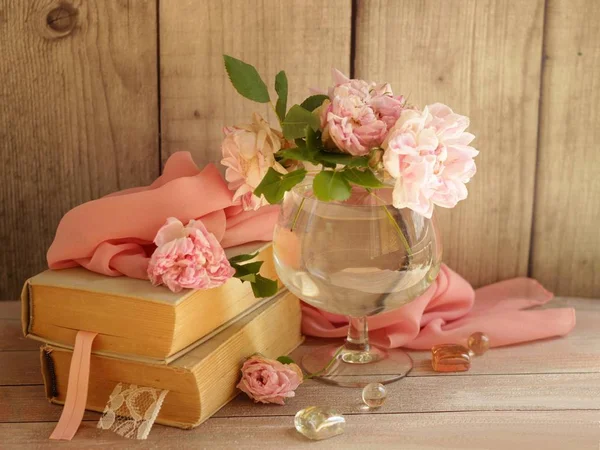 Roses roses dans un vase en verre, vieux livres, tissu de soie rose sur table en bois.Belle composition romantique shebby sur fond rustique boisé.Carte de souhaits pour mariage, anniversaire, Saint Valentin ou fête des mamans . — Photo