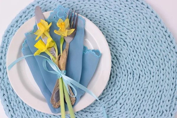 Beau décor de table de vacances de Pâques avec couverts. Fleurs narcisses, ustensiles à manger avec arc sur plaque blanche. fond de serviette tricoté aqua couleur, vue du dessus avec espace de copie . — Photo