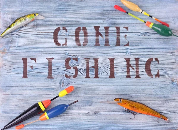 Gone fishing sign written on a pretty wooden plaque. Fishing lures and floats on rustic background.Summer fishing flat lay. Top view