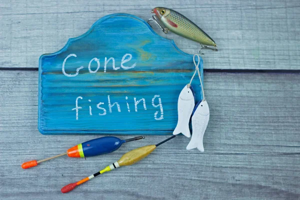 Gone fishing sign written on a pretty wooden plaque. Fishing lures and floats on rustic woody background.Summer fishing flat lay. Top view with copy space