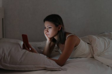 Kadın yatakta uzanıyor ve gece akıllı telefonuna bakıyor..