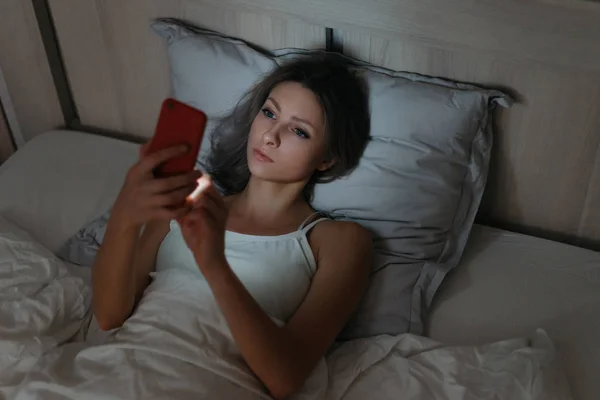 Jonge vrouw surfen op het internet met haar smartphone in bed op n — Stockfoto