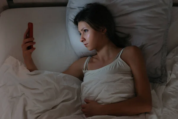 Jonge vrouw liggend in bed en met behulp van haar smartphone 's nachts. — Stockfoto