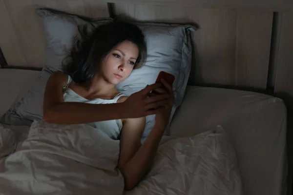 Vrouw met smartphone in bed 's nachts. — Stockfoto