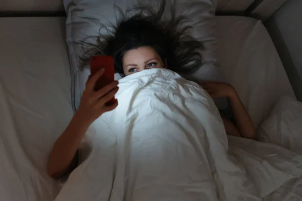 Slapende vrouw kijken naar haar smartphone in bed 's nachts. — Stockfoto