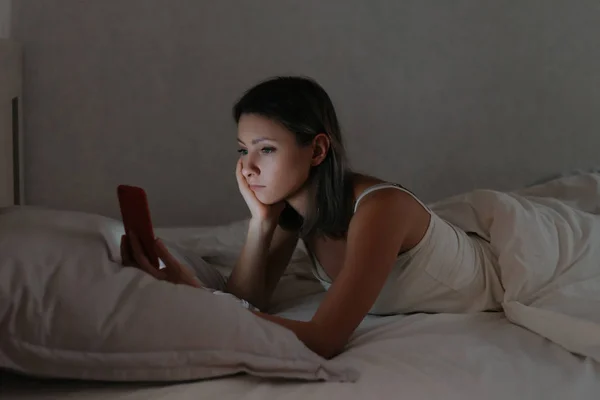 Vrouw liggend in bed en kijkend naar haar smartphone 's nachts. — Stockfoto