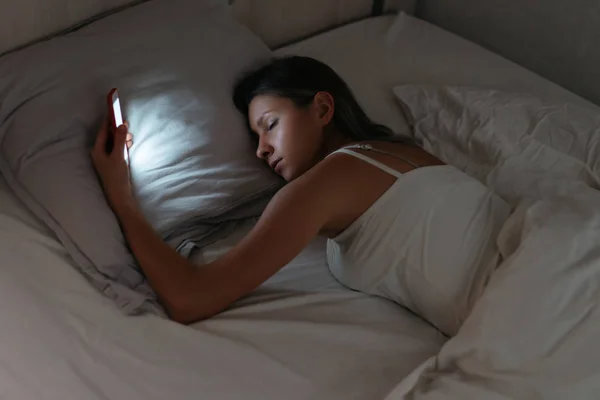 Sleeping woman is holding smartphone in her hand at night.