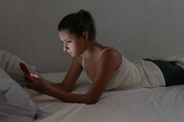 Meisje aan het chatten met haar smartphone in bed 's avonds laat. Slapeloosheid — Stockfoto