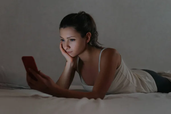 Jong vrouw met behulp van haar smartphone in bed in plaats van slaperig — Stockfoto