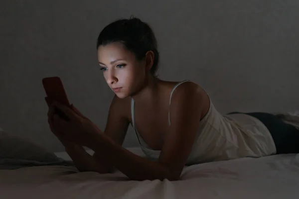 Jonge vrouw messaging met smartphone in bed 's nachts. — Stockfoto