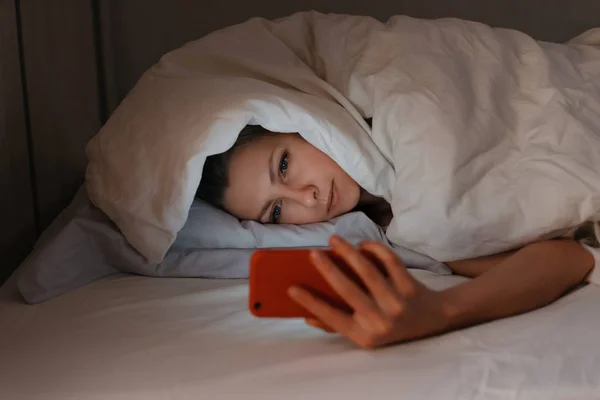 Jonge vrouw kan niet slapen en met behulp van haar smartphone in bedelen 's nachts — Stockfoto