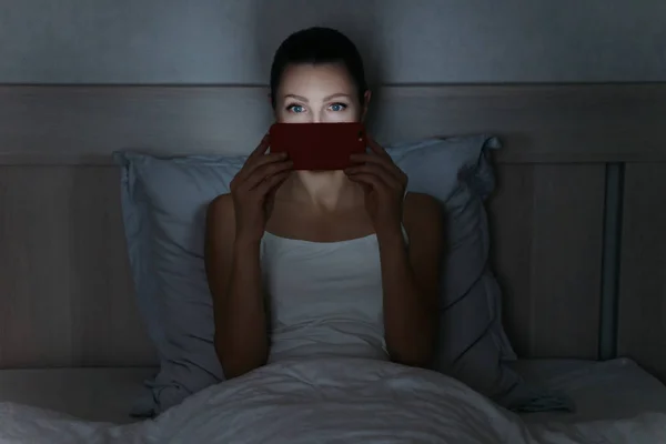 Jonge vrouw liggen in bed laat in de nacht en het houden van smartphone i — Stockfoto