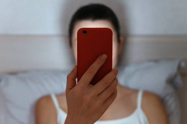 Vrouw op bed kijkt 's avonds laat naar smartphone. — Stockfoto