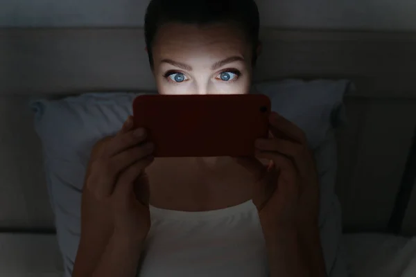 Jonge vrouw liggend op bed en verslavend staren naar haar smartph — Stockfoto