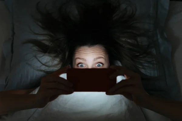 Amazed gezicht van jonge vrouw staren naar haar smartphone laat op — Stockfoto