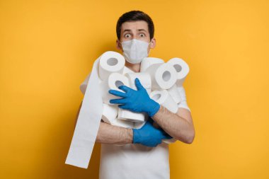 Korumalı tıbbi maske ve eldiven takan genç adam Coronavirus salgınından korkarak bir sürü tuvalet kağıdı alıyor. Covid-19 karantina, sosyal izolasyon, evde kalma konsepti. Boşluğu kopyala