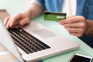 Kredi kartı tutan ve e-ticaret için dizüstü bilgisayar kullanan genç bir işadamı. İnternetten alışveriş yaparken ödeme yapmak. E-bankacılık ve modern teknoloji kavramı