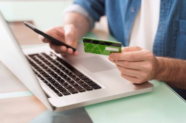 E-ticaret için akıllı telefon, dizüstü bilgisayar ve kredi kartı kullanan bir adamın ellerini kapatıyoruz. İnternetten alışveriş. E-bankacılık konsepti. Dijital Ödeme Ağı