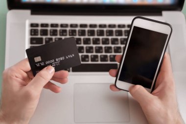 E-ticaret ve online ödeme konsepti. Genç işadamı e-bankacılık için cep telefonu ve laptop kullanıyor. Çevrimiçi döviz ticareti. İnternet sitesindeki ödemeler telefonla yapılıyor.