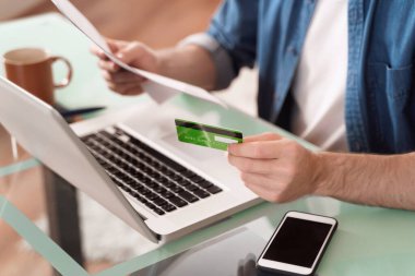 Çevrimiçi fatura ödeme kavramı. Ev faturalarını ödemek için kredi kartı ve laptop kullanan bir adam. Cep telefonuyla online alışveriş yapan genç erkeklerin yakın görüntüsü