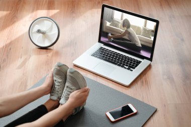 Esneklik ve güç. Genç bir kadın evde kaslarını esnetiyor, laptopta yoga dersleri izlerken egzersiz yapıyor. Fitness ve ev yoga konsepti