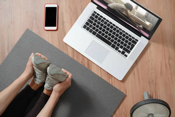 İnternetteki dersler için dizüstü bilgisayar kullanan kadınların evde bacaklarını esnetme görüntüsü. Fitness egzersizleri, sağlıklı yaşam tarzı. Koronavirüs salgını ve karantina nedeniyle evde yapılan çalışmalar. Uzaktan eğitim