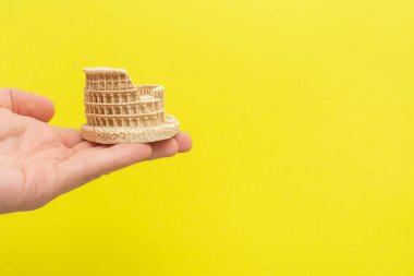 Erkek el, sarı arka planda kolezyum oyuncak modelini tutuyor. Metnin için fotokopi alanı var. İtalya 'yı gezmek ya da İtalyanca eğitimi almak