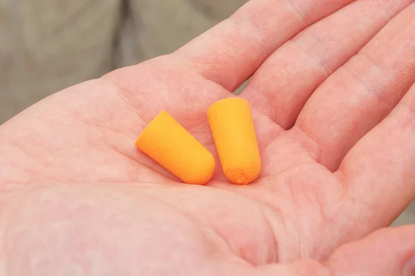 Plugues de ouvido laranja segurando na mão masculina para audição de proteção e se livrar do ruído durante o voo — Fotografia de Stock