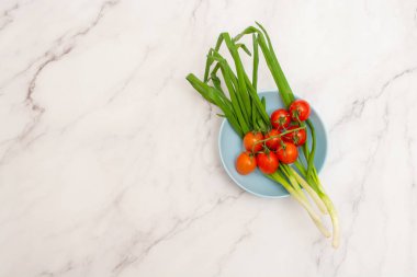 Yeşil taze soğan ve kiraz domatesli açık mavi kasenin üst görüntüsü.