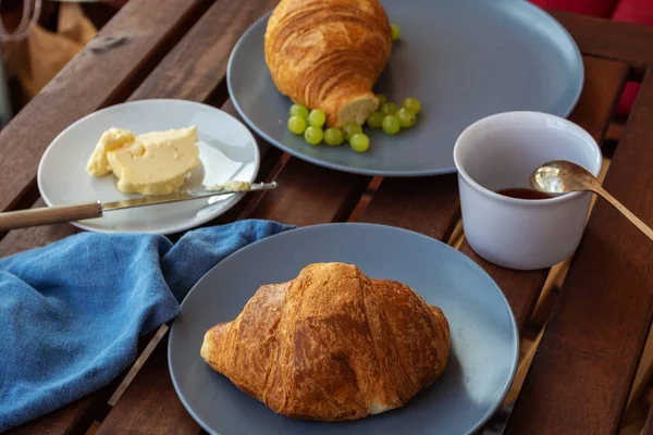 Breakfast set in French style with croissant, fruits, apples, grapes, ham, cheese and butter on grey minimalistic plates and big cup of Americano coffee