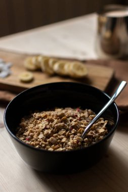 Sağlıklı kahvaltı için bir kase tahıllı yoğurt, muz dilimleri ve açık kahverengi tahta üzerinde hindistan cevizi cipsi.