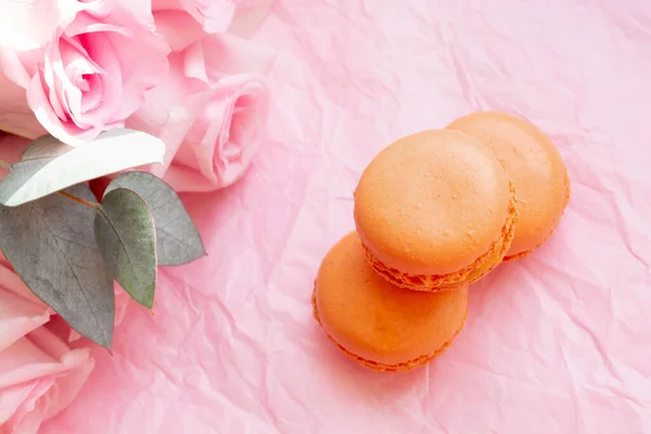 Orangefarbene Französische Makronenkekse Auf Weichem Rosa Packpapier Mit Ästhetischem Rosenstrauß — Stockfoto