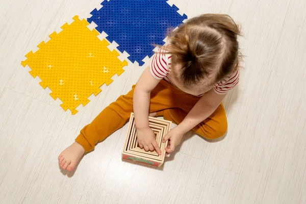 Top view of toddler girl playing with motor skill trainer cubes and puzzle massage anti flatfoot rug for developing motor skill