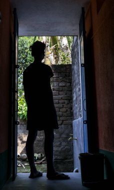 Genç bir adamın siluet görüntüsü kapının önünde duruyor ve güneşli gün ışığının ve doğanın dışına bakıyor.