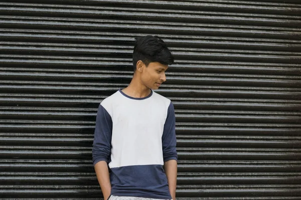 a teenager guy portrait looking down in front of a metal gate wearing white t-shirt with space for writing