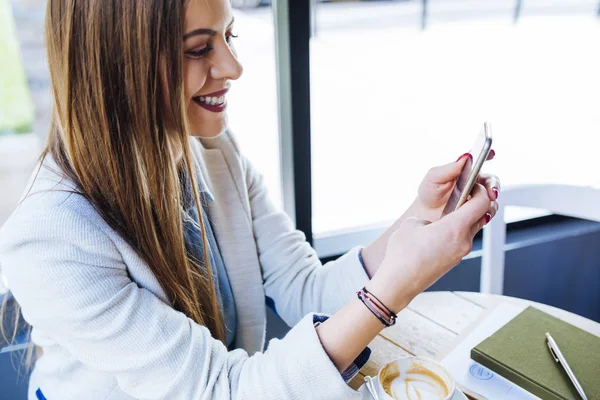 Jovem bonita sorrindo e olhando para seu telefone — Fotografia de Stock