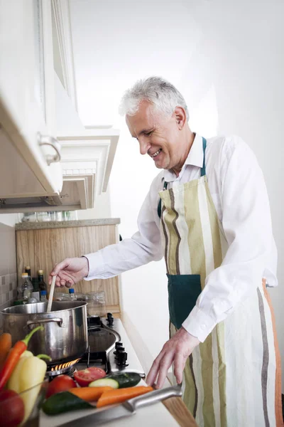 Улыбающийся пожилой человек готовит дома — стоковое фото