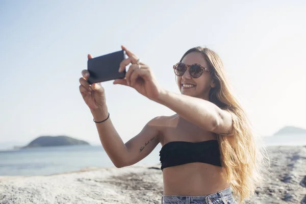 Žena s fotografii na pláži s mobilním telefonem — Stock fotografie