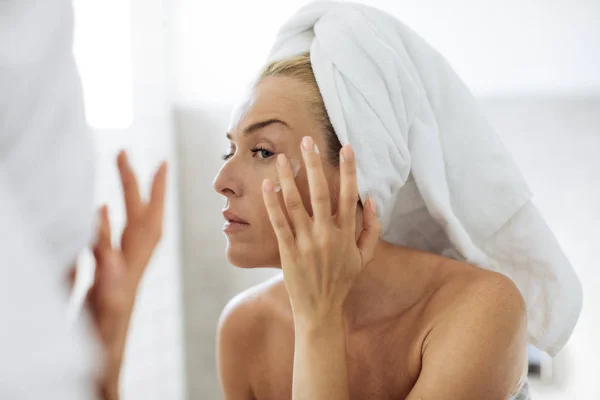 Mulher aplicando creme hidratante em seu rosto — Fotografia de Stock